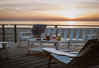 Zonsondergang bij Resort Beach Houses Julianadorp 1 in Nederland met witte stoelen, tafel en drankjes.