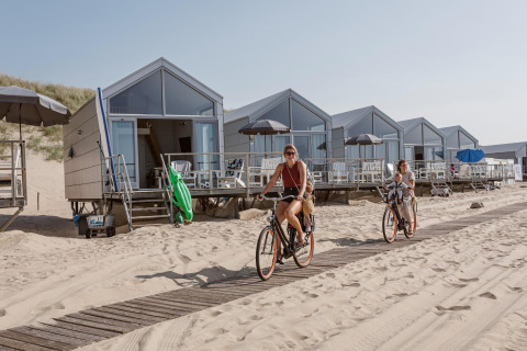 Due donne in bicicletta davanti alle case sulla spiaggia al Resort Beach Houses Julianadorp nei Paesi Bassi.