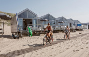Twee vrouwen fietsen langs strandhuisjes bij Resort Beach Houses Julianadorp in Nederland op een zonnige dag.