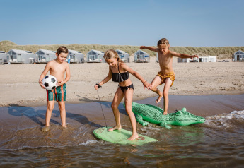 Drie kinderen spelen op het strand voor huisjes bij Resort Beach Houses Julianadorp 1 in Nederland.