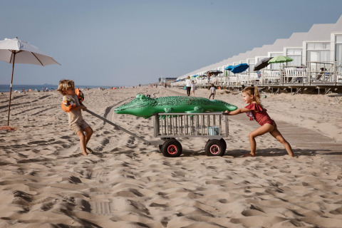 Due bambini giocano con un carrello e un coccodrillo gonfiabile sulla spiaggia di Julianadorp, Paesi Bassi.