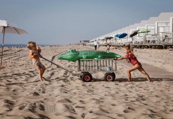 Twee kinderen spelen met een kar en een opblaaskrokodil op het strand bij strandhuizen in Julianadorp.