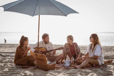Quattro amici fanno un picnic sotto un ombrellone in spiaggia al Resort Beach Houses Julianadorp 1, Olanda.