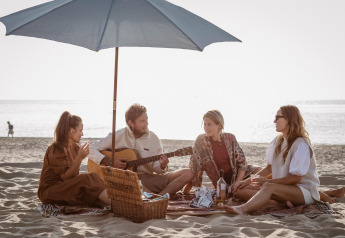 Vier vrienden picknicken onder een parasol op het strand bij Resort Beach Houses Julianadorp 1, Nederland.