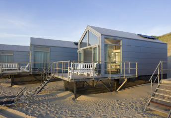 Moderne strandhuisjes op palen bij Resort Beach Houses Julianadorp in Nederland, met zand en terrassen.