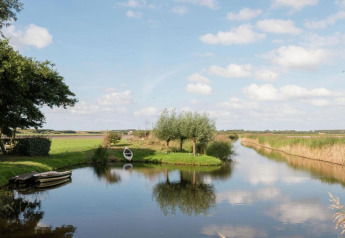 Sfeervol landschap bij Resort Beach Houses Julianadorp in Nederland, met bootjes en groene velden bij water.