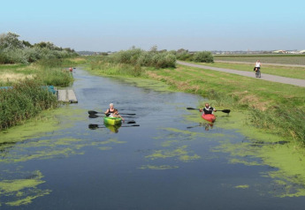 Twee mensen kayakken in een smalle sloot bij Resort Beach Houses Julianadorp in Nederland.