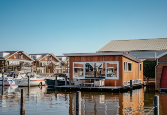 Houseboat named Waterpark de Meerparel 5 docked among boats, modern homes in background, calm sunny day.