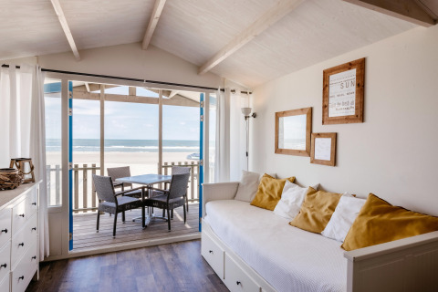 Bright living room in a beach house with ocean view, white sofa, yellow pillows, and outdoor seating.