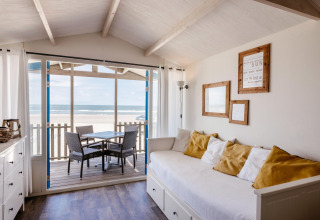 Bright living room in a beach house with ocean view, white sofa, yellow pillows, and outdoor seating.