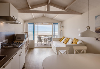 Bright beach house with open kitchen, sofa with cushions, and terrace overlooking the sea view.