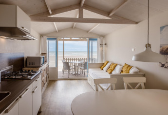 Licht strandhuis met open keuken, bank met kussens en terras met uitzicht op zee op de achtergrond.