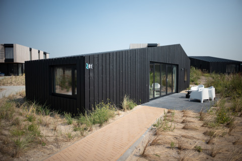 Casa de playa negra moderna en Sea Lodges Zandvoort, Países Bajos, rodeada de dunas y muebles de exterior.