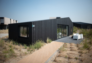 Casa de playa negra moderna en Sea Lodges Zandvoort, Países Bajos, rodeada de dunas y muebles de exterior.
