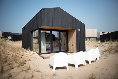Casa de playa negra moderna Sea Lodges Zandvoort 3 con puertas de cristal y sillas blancas en dunas.