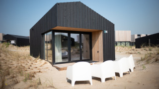 Casa de playa negra moderna Sea Lodges Zandvoort 3 con puertas de cristal y sillas blancas en dunas.