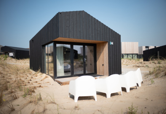 Casa de playa negra moderna Sea Lodges Zandvoort 3 con puertas de cristal y sillas blancas en dunas.