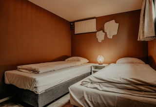 Acogedor dormitorio en el houseboat Waterpark «de Meerparel 5» con dos camas individuales y luz cálida.