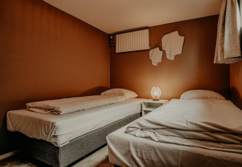 Cozy twin bedroom on the Waterpark «de Meerparel 5» houseboat with warm light and brown walls.