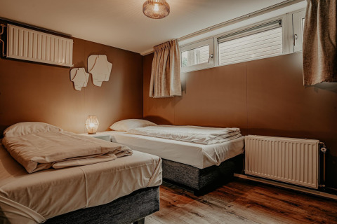 Modernes Schlafzimmer mit zwei Einzelbetten, brauner Wand und Fenstern, Waterpark de Meerparel 5, Niederlande.