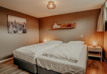 Cozy bedroom with two single beds, bedside lamps, and modern wall art in Waterpark de Meerparel 5 houseboat.