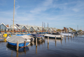 Både fortøjet ved en havn foran moderne glampinghytter under en blå himmel, fredeligt miljø.