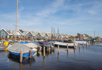 Boats docked in a marina in front of modern glamping accommodations with a clear blue sky above.