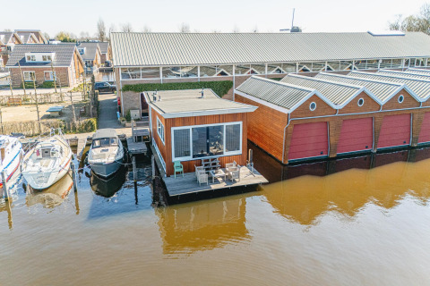 Udsigt over husbåd Waterpark de Meerparel 5 med terrasse, både og pakhus i Holland ved vandet.