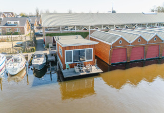 Udsigt over husbåd Waterpark de Meerparel 5 med terrasse, både og pakhus i Holland ved vandet.