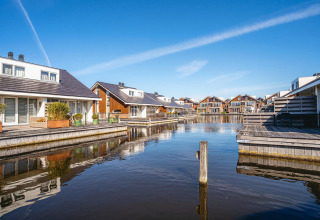 Hyggelige hytter ved vandet på et glamping-resort med træterrasser og blå himmel i baggrunden.