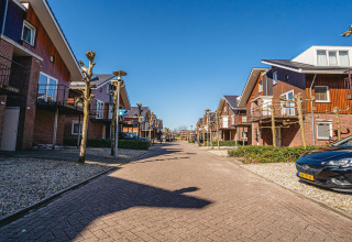 Moderne Glamping-Unterkünfte an einer ruhigen Straße, Holzhäuser und Autos unter klarem Himmel.