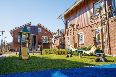 Legeplads med rutsjebane og vippe foran moderne huse ved Waterpark de Meerparel 5 i Holland på en solrig dag.