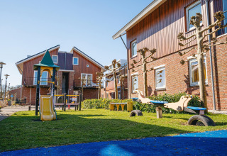 Spielplatz mit Rutsche und Wippe vor modernen Häusern im Waterpark de Meerparel 5 in den Niederlanden.