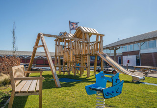 Parque infantil con tobogán y columpios en un alojamiento glamping, junto a bancos y edificios modernos.