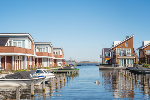 Moderne huizen aan het water met steigers en boten bij een glamping accommodatie op een zonnige dag.