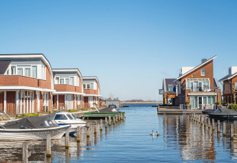 Modern waterfront houses with private docks and boats at a luxury glamping accommodation on a sunny day.