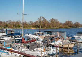 Boats and houseboats docked at a glamping marina on a sunny day with trees in the background.