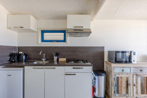 Modern beach house kitchenette with stove, microwave, fridge and coffee makers on the countertop.