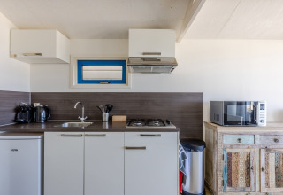 Modern beach house kitchenette with stove, microwave, fridge and coffee makers on the countertop.