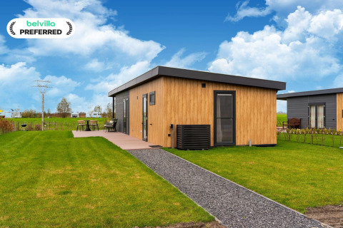 Modern lodge at 'By the Baker' in the Netherlands with wood siding, patio set, and scenic green lawn outdoors.