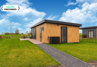 Modern lodge at 'By the Baker' in the Netherlands with wood siding, patio set, and scenic green lawn outdoors.