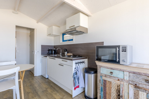 Bright, modern kitchenette in a beach house with gas stove, microwave, sink, and rustic cabinet.