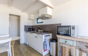 Lichte, moderne kitchenette in een strandhuis met gasfornuis, magnetron, wasbak en rustiek kastje.