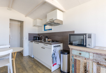 Lichte, moderne kitchenette in een strandhuis met gasfornuis, magnetron, wasbak en rustiek kastje.