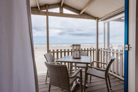 View from a beach house patio with four chairs and a table, overlooking the sandy beach and ocean waves.
