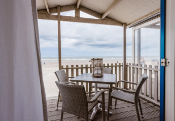 Uitzicht vanaf een strandhuis terras met vier stoelen en tafel op het zandstrand en de zee onder wolken.