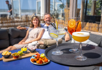 Een stel ontspant bij een strandpaviljoen met kleurrijke cocktails en hapjes, op een zonnige dag aan zee.