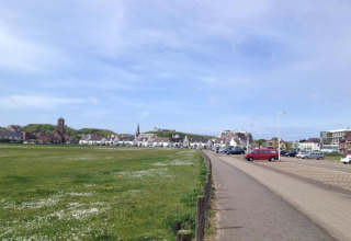 View from a beach house showing grass, a parking lot with cars, and a village under a clear blue sky.