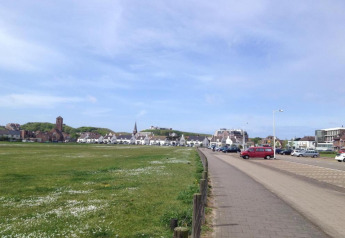Uitzicht vanaf een strandhuis met grasveld, parkeerplaats, geparkeerde auto's en huizen onder blauwe lucht.