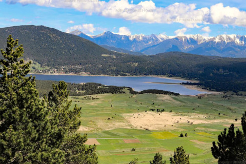Blick auf einen See, grüne Felder und schneebedeckte Berge von einer Glamping-Unterkunft aus.